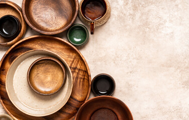Many different ceramic and wooden plates and bowls on a beige background top view. Flat lay. Background from empty plates and bowls. Free space for text. Various empty dishes.