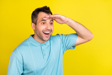 Fototapeta na wymiar Photo of funny brunet man look far wear blue t-shirt isolated on yellow color background