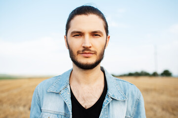 Outdoor portrait of handsome young man in denim jacket, in the field.