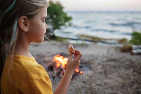 Cute Girl Roasting Marshmallow To Make Smores Over Fire Flame During Camping, Traditional American Food, Active Recreation And Family Travel