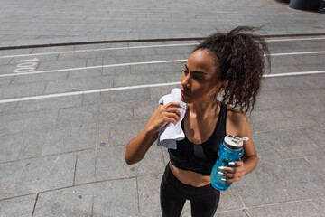 High angle view of african american woman in sportswear holding sports bottle and towel outdoors