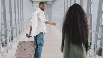 Back view multiracial couple unrecognizable curly brunette woman and african man with luggage suitcase in airport afro guy boarding plane travel holding passport tickets turns waving goodbye to girl
