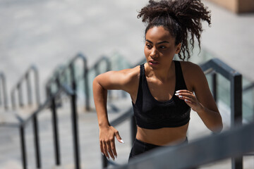 Pretty african american sportswoman running on blurred stairs