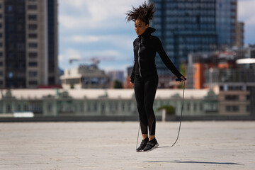 African american sportswoman jumping with rope on urban street