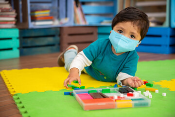 Mexican baby in school with face mask playing with colored pieces on a mat, back to school 