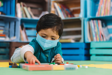 Mexican baby at school with face mask playing with colored pieces on a mat back to school 