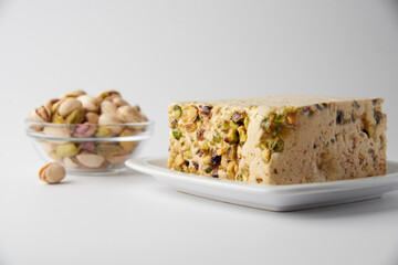 Organic halva with pistachios on a white plate isolated on white. Traditional middle eastern sweets. Jewish, turkish, arabic oriental national dessert. Turkish delight concept. Natural vegan product.