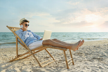 Happy man with laptop talking by mobile phone on beach. Business trip