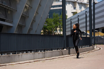 Side view of african american sportswoman running near building on urban street