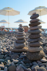 The process of building a pyramid of stones. A close-up hand places the top stone on top of the pyramid. Rays of the setting sun. The concept of calm.