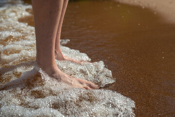 A man standing on the clean sandy beach with wave motion coming to the feet.