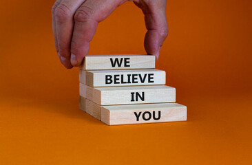 We believe in you symbol. Concept words 'We believe in you' on wooden blocks on a beautiful orange background. Businessman hand. Business, religion and we believe in you concept.