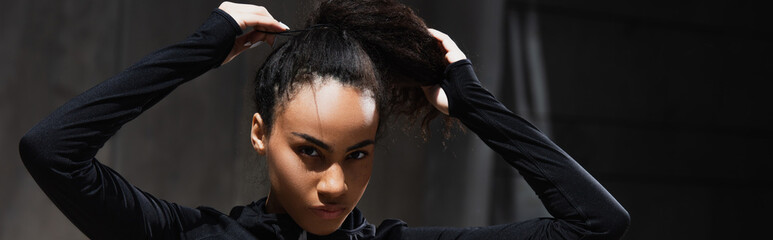 African american sportswoman adjusting hair and looking at camera outdoors, banner