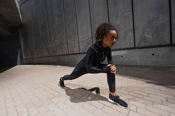 Pretty african american sportswoman stretching legs on urban street
