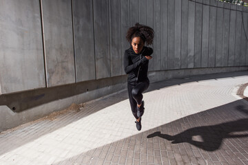 African american sportswoman looking at camera while running on urban street