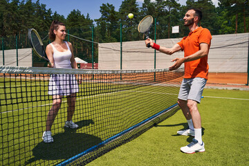 Joyous cute sportsman serving the ball to his tennis partner