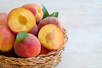 Naklejka na ściany i meble Bunch of ripe organic peaches in a wicker bowl, white wooden table background. Local produce fruits in a basket. Clean eating concept. Top view, close up, copy space for text.