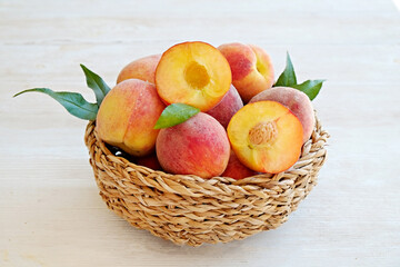 Bunch of ripe organic peaches in a wicker bowl, white wooden table background. Local produce fruits in a basket. Clean eating concept. Top view, close up, copy space for text.