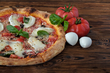 Cropped shot of oven baked pizza with buffalo mozzarella, parmigiano-reggiano cheese, basil and anchovies. Traditional italian dish on wood textured table background. Close up, copy space, top view.