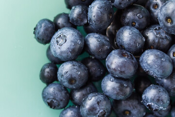 A lot of beautiful juicy fresh summer blueberries on a light turquoise glass plate
