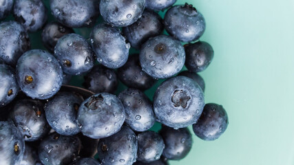A lot of beautiful juicy fresh summer blueberries on a light turquoise glass plate