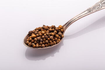 coriander seeds in a cupronickel spoon on white background