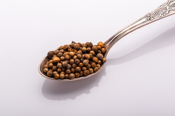 coriander seeds in a cupronickel spoon on white background