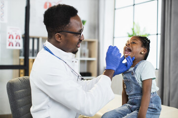Lovely little afro-american child girl sitting on the couch at doctor's office, while handsome...