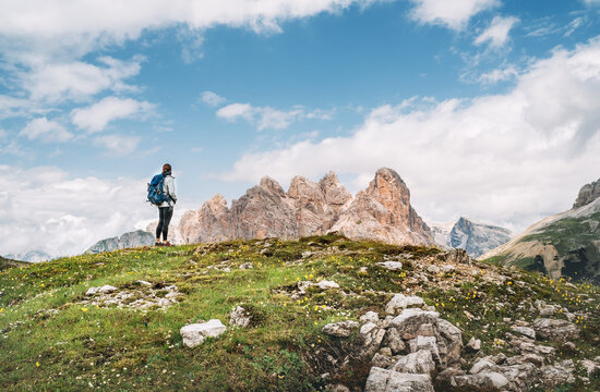 Woman trekker with backpack and trekking poles on green hill enjoying picturesque Dolomite Alps view near Tre Cime di Lavaredo formation in South Tyrol, Italy. Active people and mountain concept.