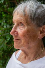 Portrait of mature woman in her garden. Close-up of expressive elderly woman. Portrait of female model posing outdoor.