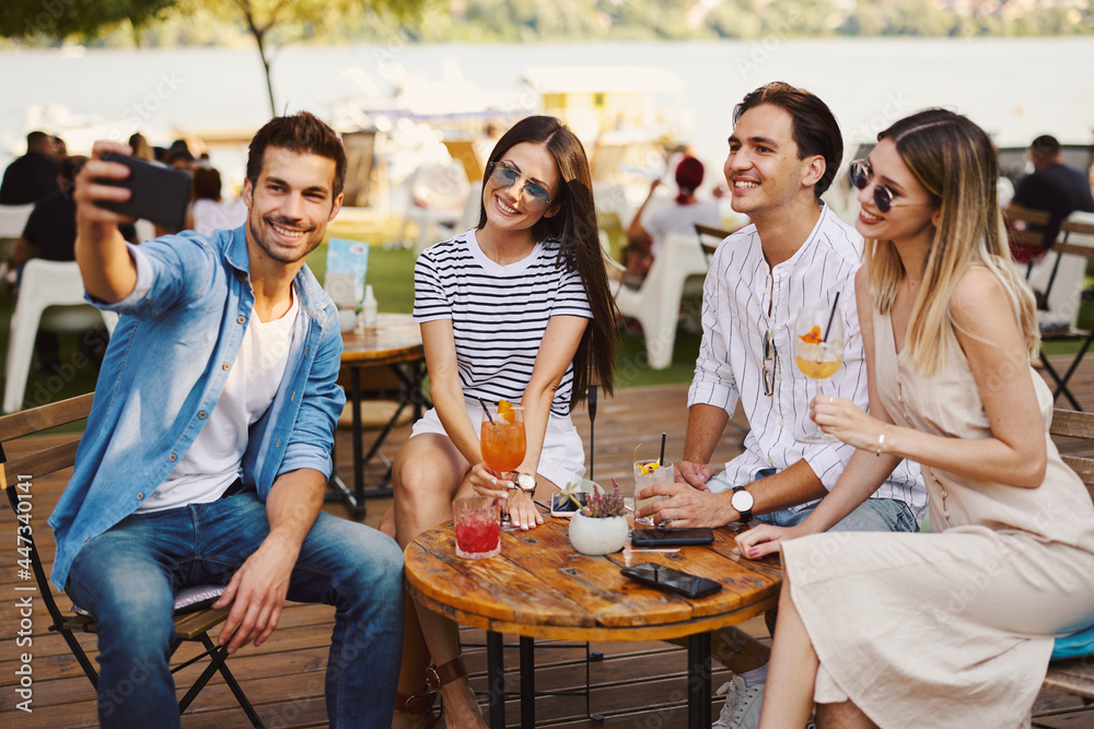 Sticker Group of young happy people drinking cocktails and taking selfies at a summer bar