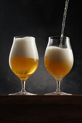 Two glass of light yellow beer on dark background. Selective focus
