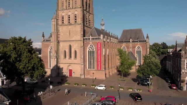 Aerial descend revealing a square in front of the Walburgiskerk cathedral with people passing by and a large red banner of the World Press Photo on exterior facade. Architecture cultural heritage.