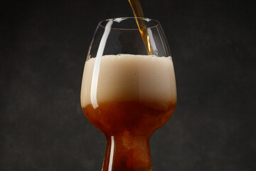 Beer with flowing foam head. Stream of stout pours into a beer glass. Selective focus
