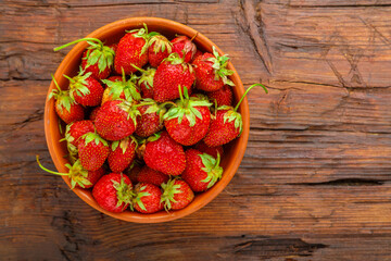 Ripe strawberries in a clay plate on a wooden table.