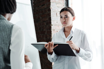 Asian girl student in a white shirt holds a notebook in her hands and writes down under the...