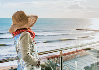 a woman in a hat contemplates the autumn sunset from a terrace on the coast.