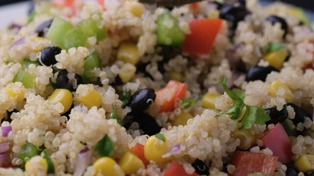 Picking Quinoa black bean salad with corn, red green pepper, onion, using a tablespoon. Healthy food.