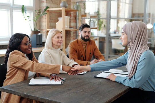 Happy African businesswoman shaking hand of Muslim female applicant after interview