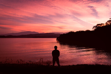 Obraz premium silhouette of a man on the shore of a lake during sunset