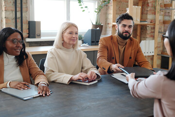 Young bearded businessman passing folder with contract to Asian female applicant