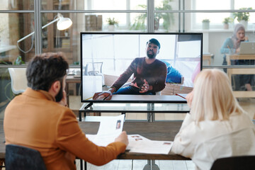 Obraz premium Confident male applicant on large display talking to employers in office during online interview