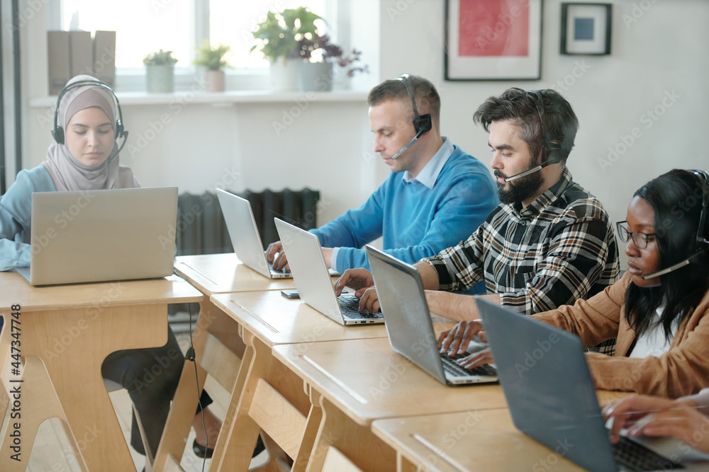 Poster young intercultural customer support representatives working in front of laptops in office