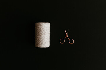 A spool of white cotton rope, and a rose gold scissors on black background.