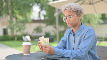 African Woman Counting Dollars in Outdoor Cafe