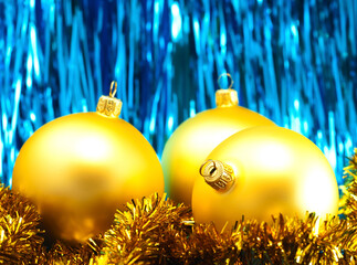 Yellow Christmas baubles with golden tinsel on a shiny blue background