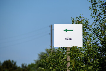 A sign with a directional arrow and an indication of 150 meters. The background is a bush, the sky and power lines