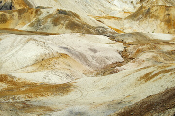Hilly, lifeless landscape. The hills are composed of brown clay and sand. On the left, there are traces of human feet and motorcycle wheels on the ground. Desert landscape. Copy space.