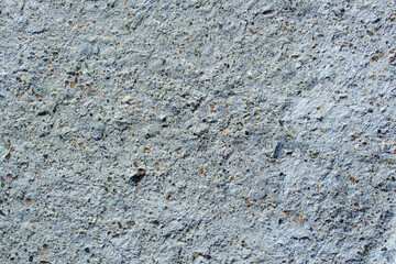 Flat surface of gray concrete. The material has pores, inclusions of brown and brown rubble. The surface is rough and rough. Texture close-up view.