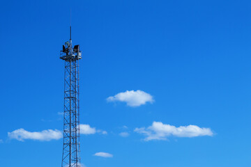 A tall, metal tower with powerful floodlights against a backdrop of blue sky and clouds. The tower stands upright. The structure serves to illuminate the area at night.